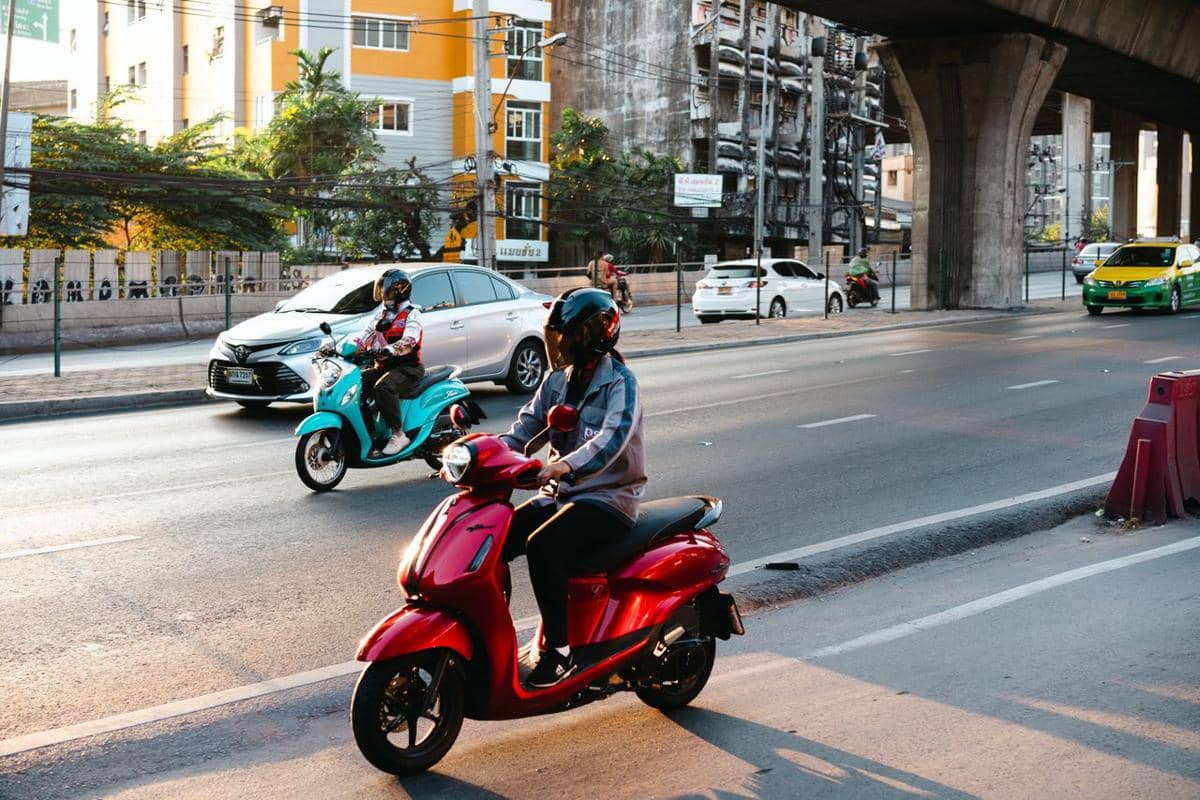 Beberapa pengendara motor mengenakan helm melintas di jalan perkotaan dengan lalu lintas kendaraan di bawah jembatan layang.