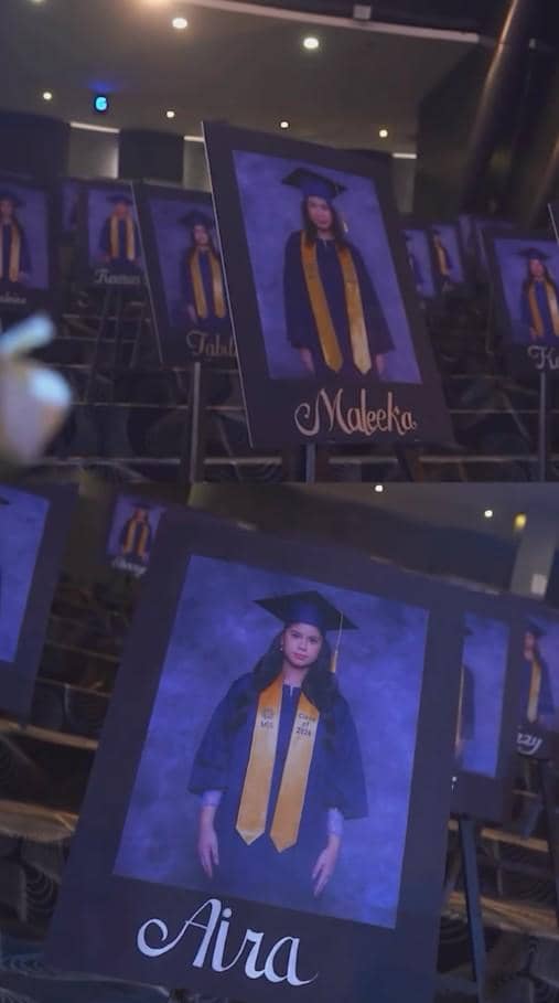 Potret kelulusan siswa SMA dengan toga dan selempang kuning dipajang di atas papan, menampilkan suasana acara wisuda di aula.