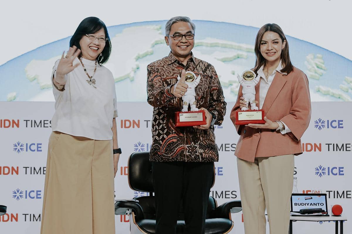 Tiga pembicara tersenyum di panggung Indonesia Summit 2025 sambil memegang trofi penghargaan dengan latar belakang logo IDN Times dan ICE.