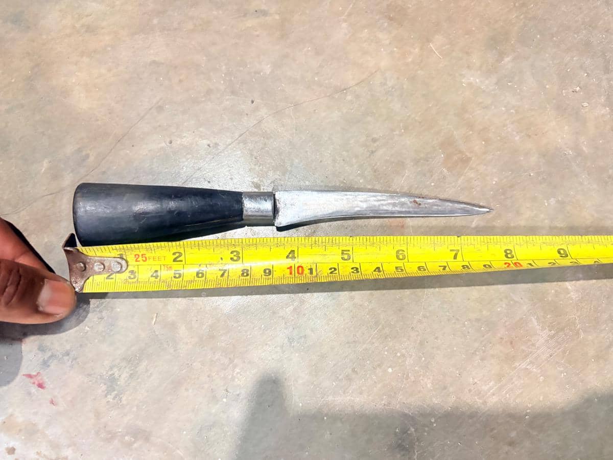 Pisau dengan gagang hitam diukur menggunakan meteran kuning di atas lantai, diduga sebagai barang bukti dalam penyelidikan polisi.