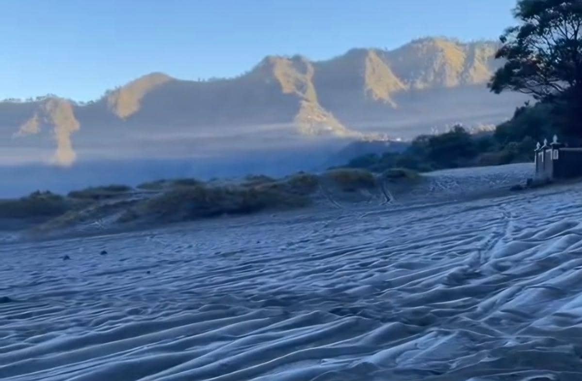 Permukaan pasir di kawasan Gunung Bromo tampak diselimuti embun upas dengan latar pegunungan dan langit biru di pagi hari.