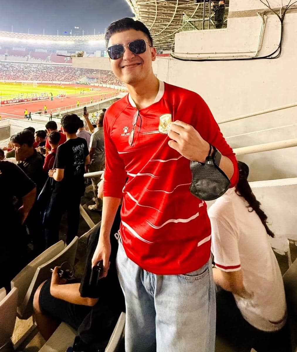 Seorang pria mengenakan jersey merah timnas Indonesia berdiri di tribun Stadion GBK saat menonton pertandingan melawan Mozambik.