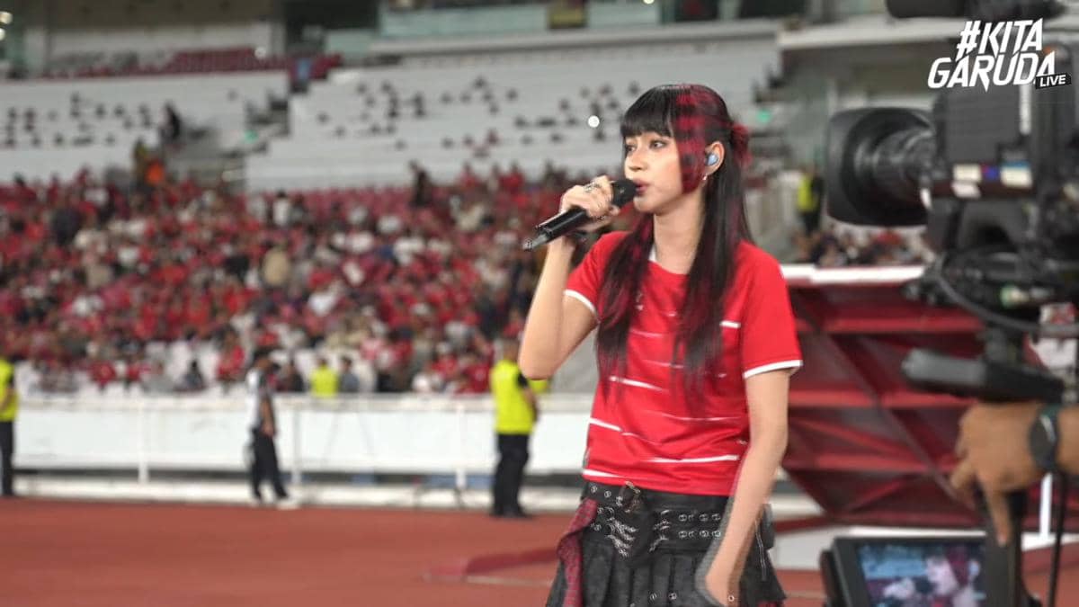 Seorang penyanyi mengenakan kaus merah sedang bernyanyi di stadion di depan penonton sebelum pertandingan timnas Indonesia versus Mozambik.