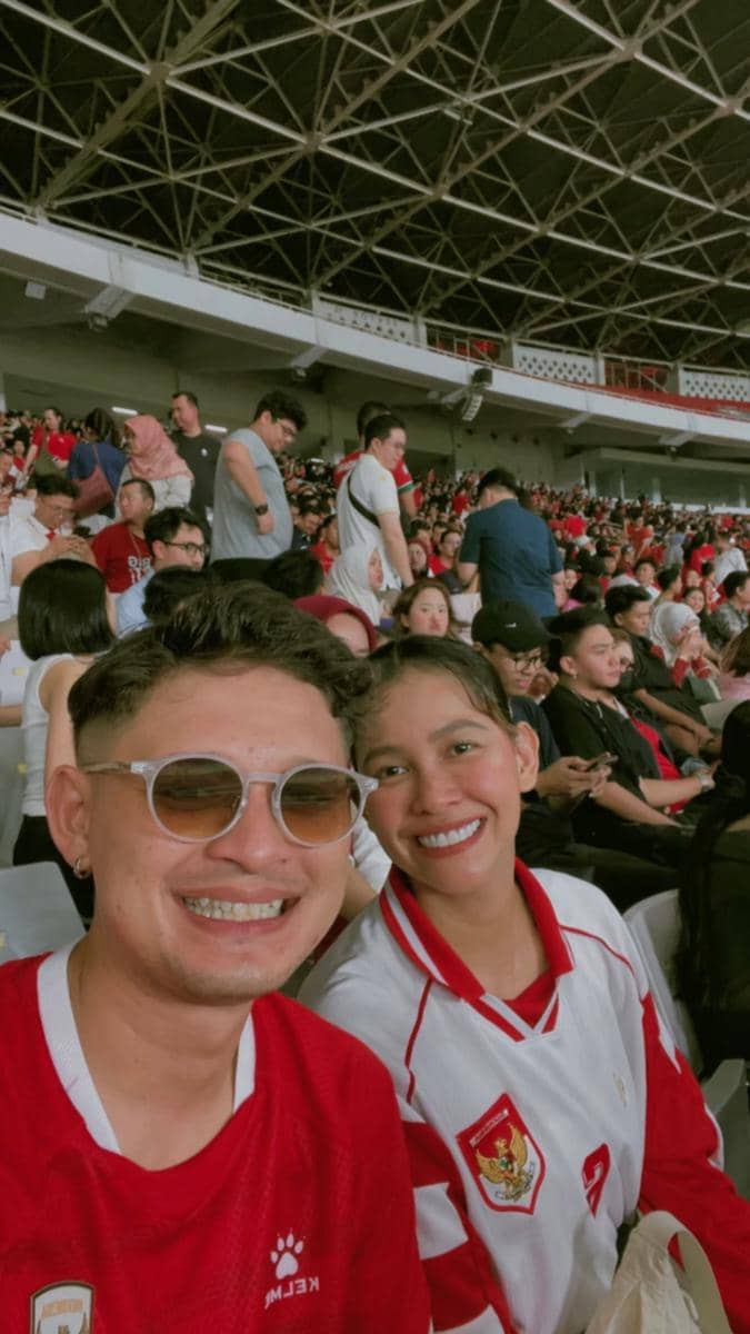 Dua penonton mengenakan jersey timnas Indonesia tersenyum di tribun Stadion Gelora Bung Karno saat laga melawan Mozambik.