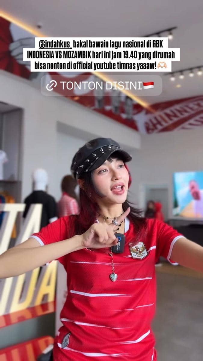 Seorang perempuan mengenakan jersey merah timnas Indonesia dan topi hitam berpose sambil menunjuk, menjelang laga Indonesia vs Mozambik.