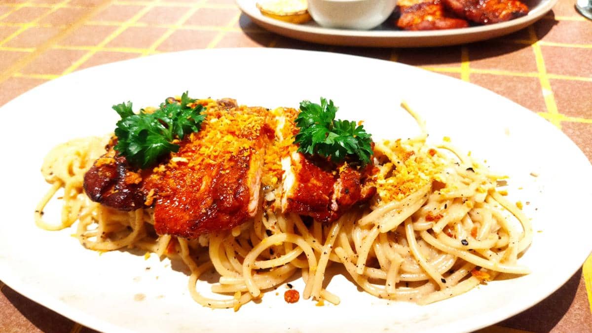 Sepiring spaghetti dengan saus krim disajikan bersama potongan ayam panggang berwarna kecokelatan dan taburan parsley segar.