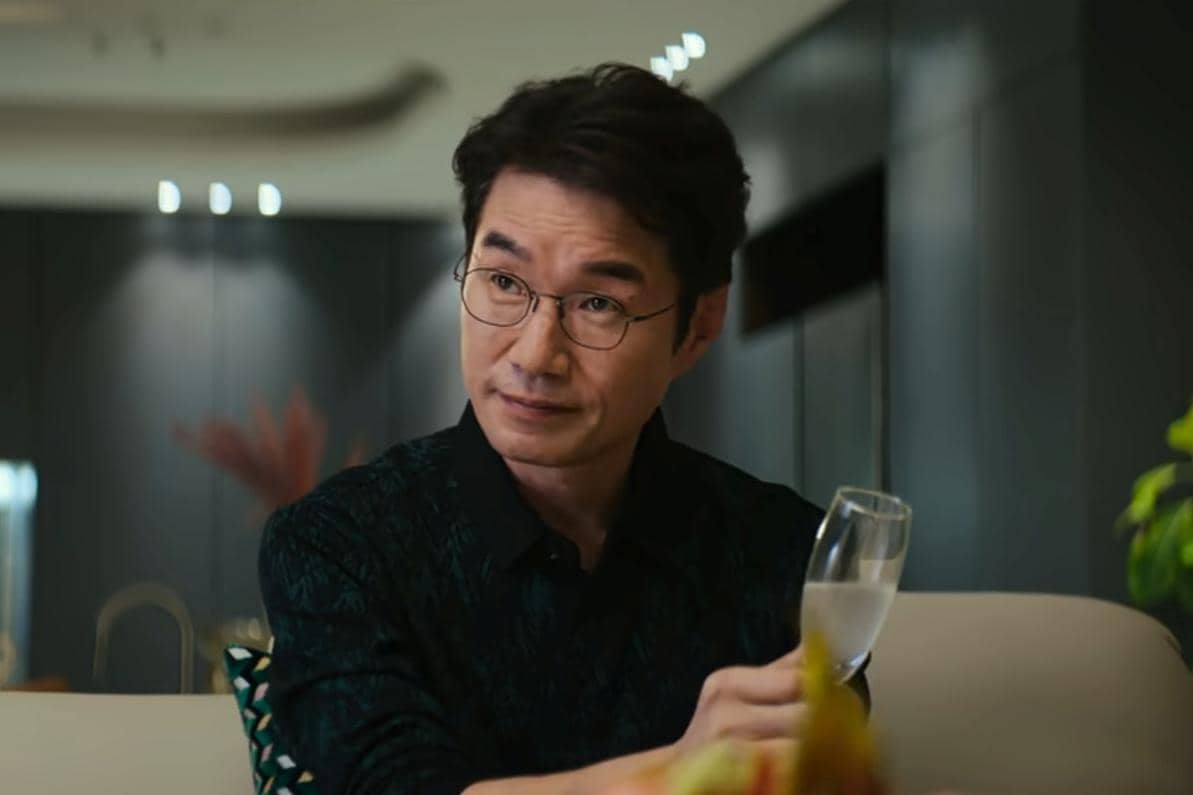 Song Young Kyu duduk di ruang modern sambil memegang gelas minuman dalam adegan drama Korea Teach You a Lesson.