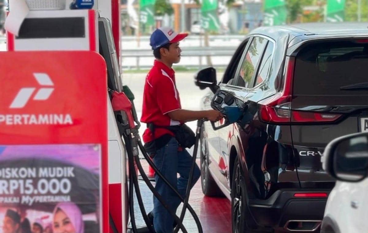 Petugas SPBU Pertamina mengenakan seragam merah sedang mengisi bahan bakar ke mobil hitam di pom bensin Pertamina.