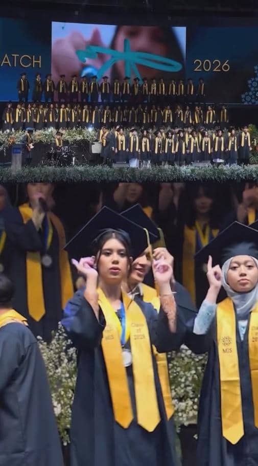 Para siswa mengenakan toga dan selempang kuning saat upacara wisuda SMA angkatan 2026 di atas panggung dengan latar layar besar.