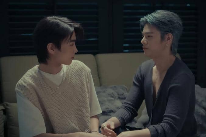 Dua pria duduk berhadapan di sofa dalam suasana redup, saling menatap dengan ekspresi serius dalam cuplikan drama The Crow Club.