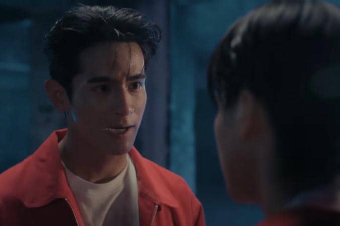 Seorang pria mengenakan jaket merah berbicara serius dengan seseorang di depannya dalam adegan drama The Crow Club.