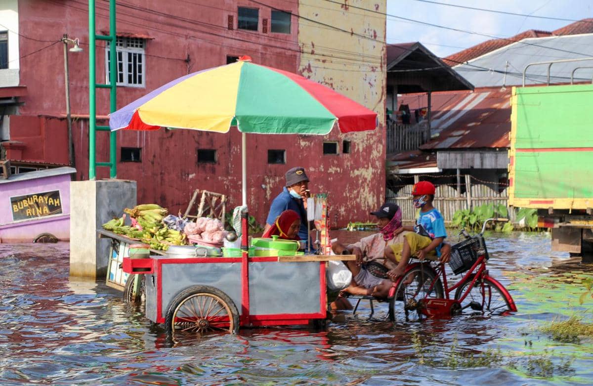 Ilustrasi gerobak makanan kaki lima di jalan yang tergenang banjir.