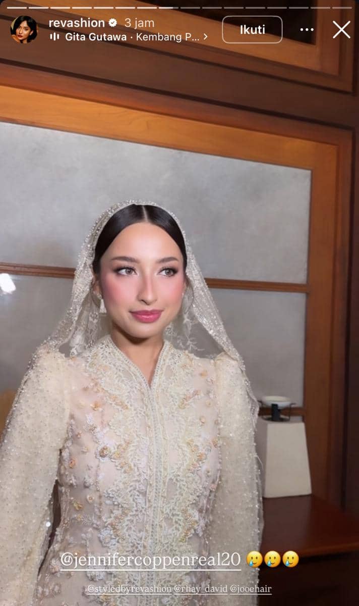 Seorang perempuan mengenakan kebaya krem berhias payet dan kerudung renda, berdiri di dalam ruangan dengan pencahayaan hangat.