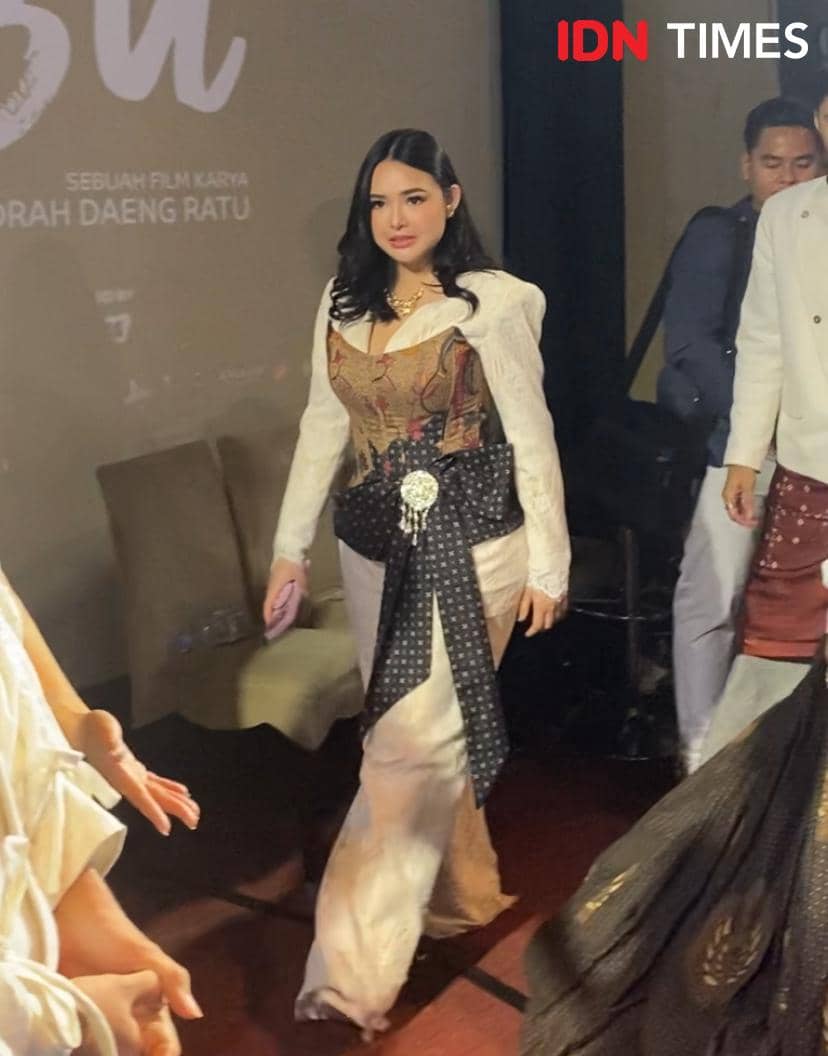 Seorang perempuan mengenakan kebaya modern berwarna putih dan batik berjalan di acara premier film di XXI Plaza Indonesia.