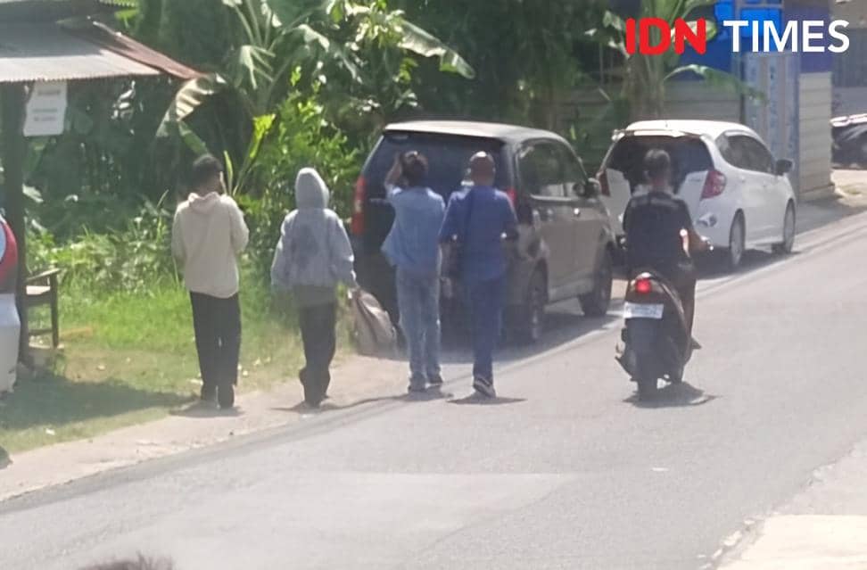 Beberapa orang berjalan di pinggir jalan dekat mobil yang terparkir, salah satunya tampak mengangkat tangan saat diamankan setelah rekonstruksi.