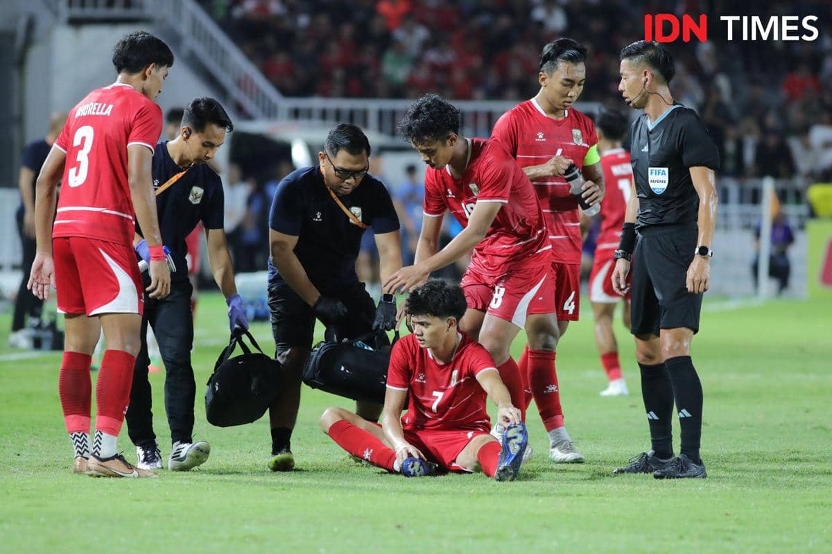 Pemain Timnas Indonesia U-19 duduk di lapangan setelah mengalami cedera saat laga Piala AFF U-19, dibantu rekan setim dan tim medis.