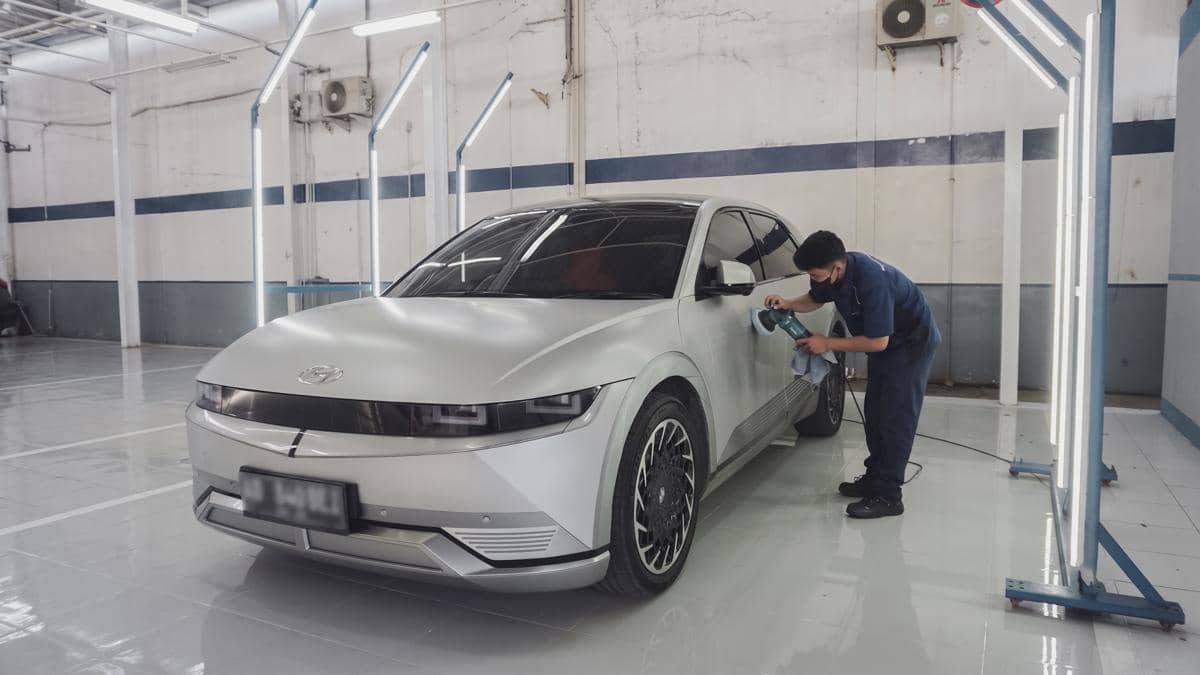 Seorang teknisi sedang memoles bodi mobil listrik berwarna silver di bengkel modern dengan pencahayaan terang di Jawa Tengah.