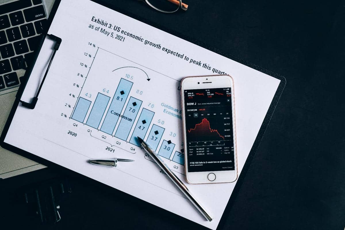 Grafik pertumbuhan ekonomi AS di atas kertas dengan ponsel menampilkan data pasar saham dan pena di atas meja kerja.
