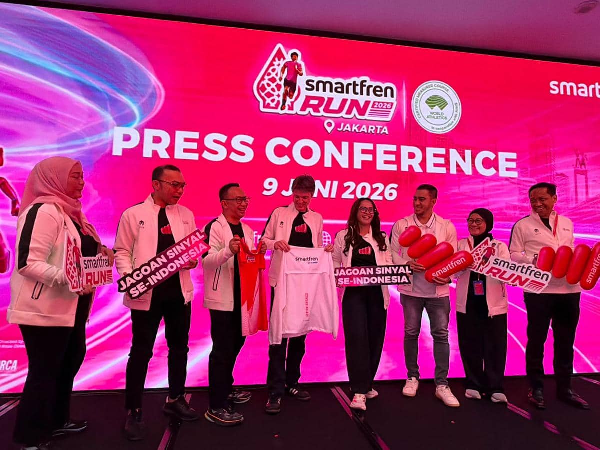 Perwakilan Mills dan Smartfren berpose bersama dalam konferensi pers Smartfren Run 2026 di Jakarta dengan latar merah muda cerah.