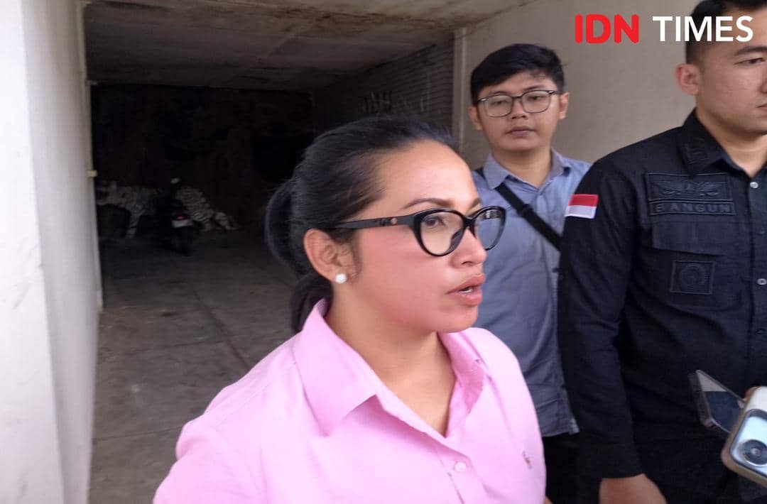 Seorang perempuan berbaju merah muda berbicara kepada media didampingi dua pria di area luar gedung setelah rekonstruksi kasus.