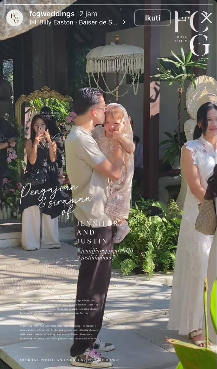 Seorang pria mencium anak kecil yang mengenakan gaun berenda dalam acara pengajian dan siraman menjelang pernikahan di area outdoor.