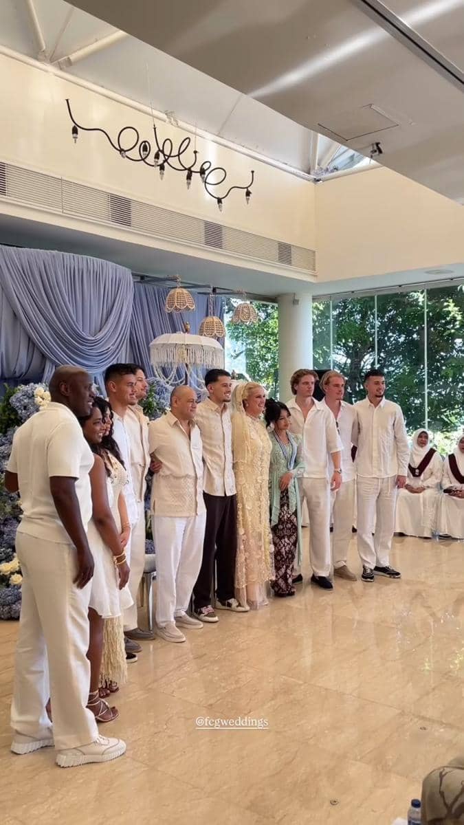 Keluarga berpose bersama dalam acara pengajian dan siraman dengan busana serba putih di ruangan berhias tirai dan lampu gantung.