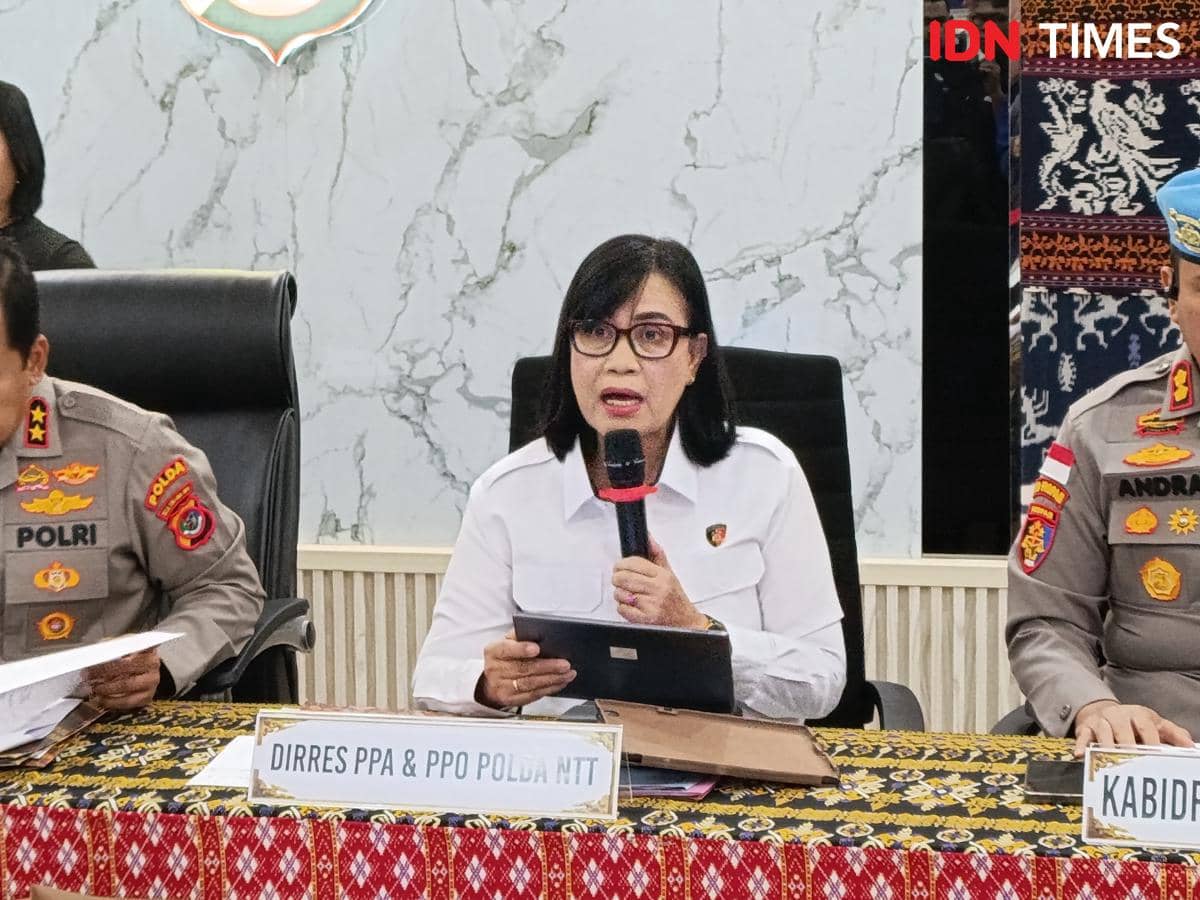 Seorang pejabat kepolisian berpakaian putih berbicara memegang mikrofon di antara dua perwira polisi berseragam saat konferensi pers.