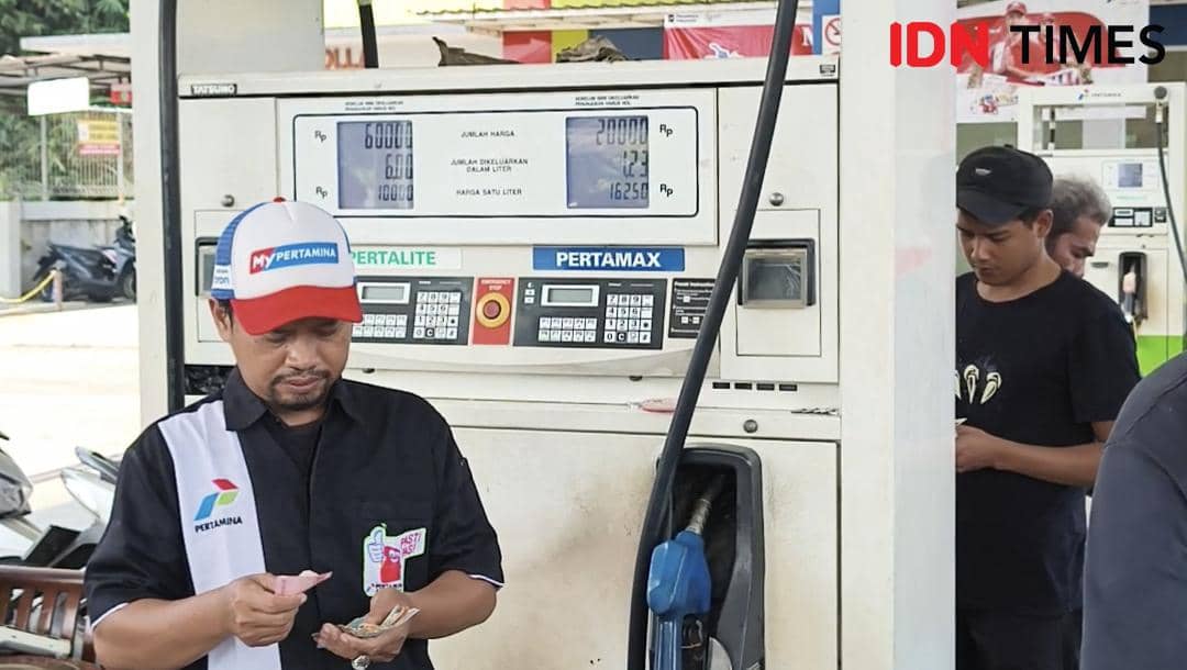 Petugas SPBU mengenakan seragam Pertamina menghitung uang di depan pompa bensin dengan latar belakang dispenser Pertalite dan Pertamax di Kota Bogor.