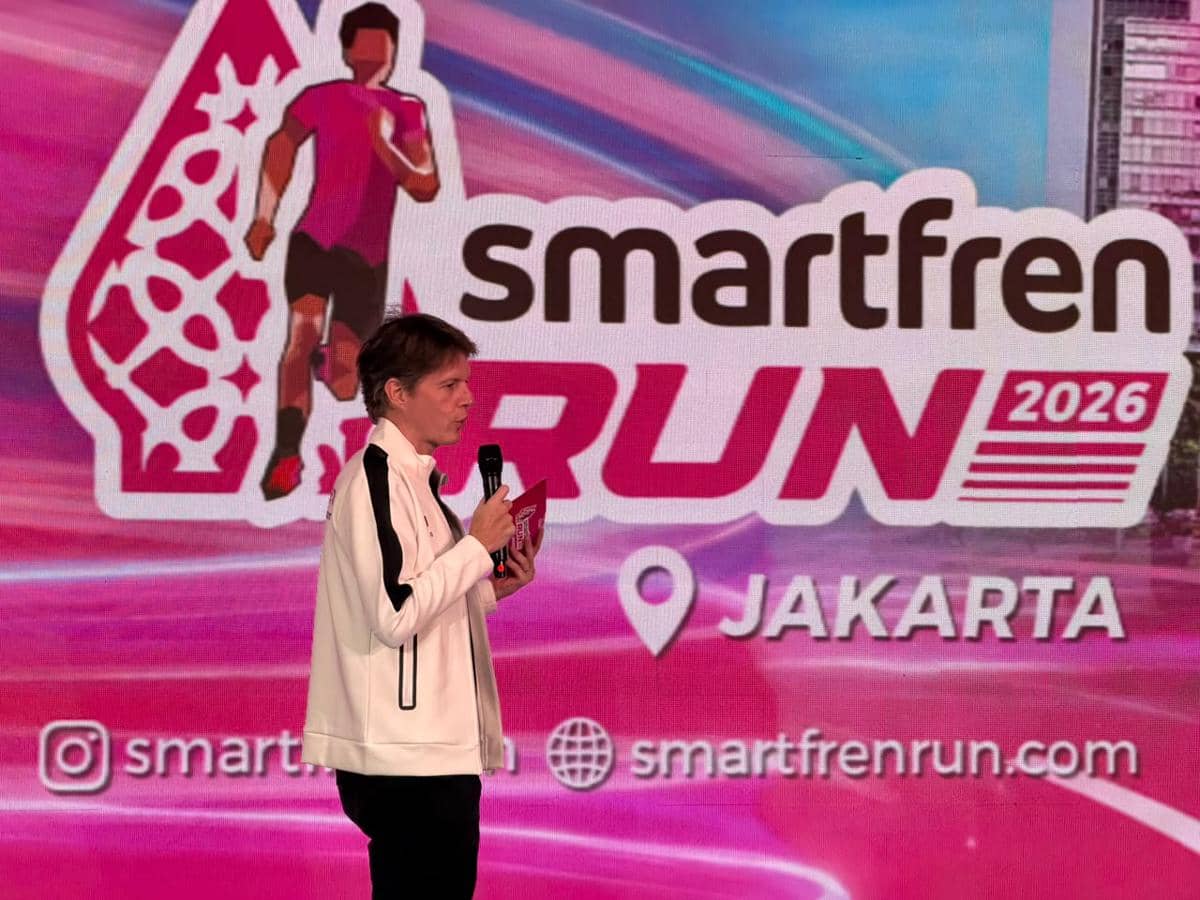 Seorang pembicara mengenakan jaket putih berbicara di atas panggung dengan latar belakang logo Smartfren Run 2026 di Jakarta.