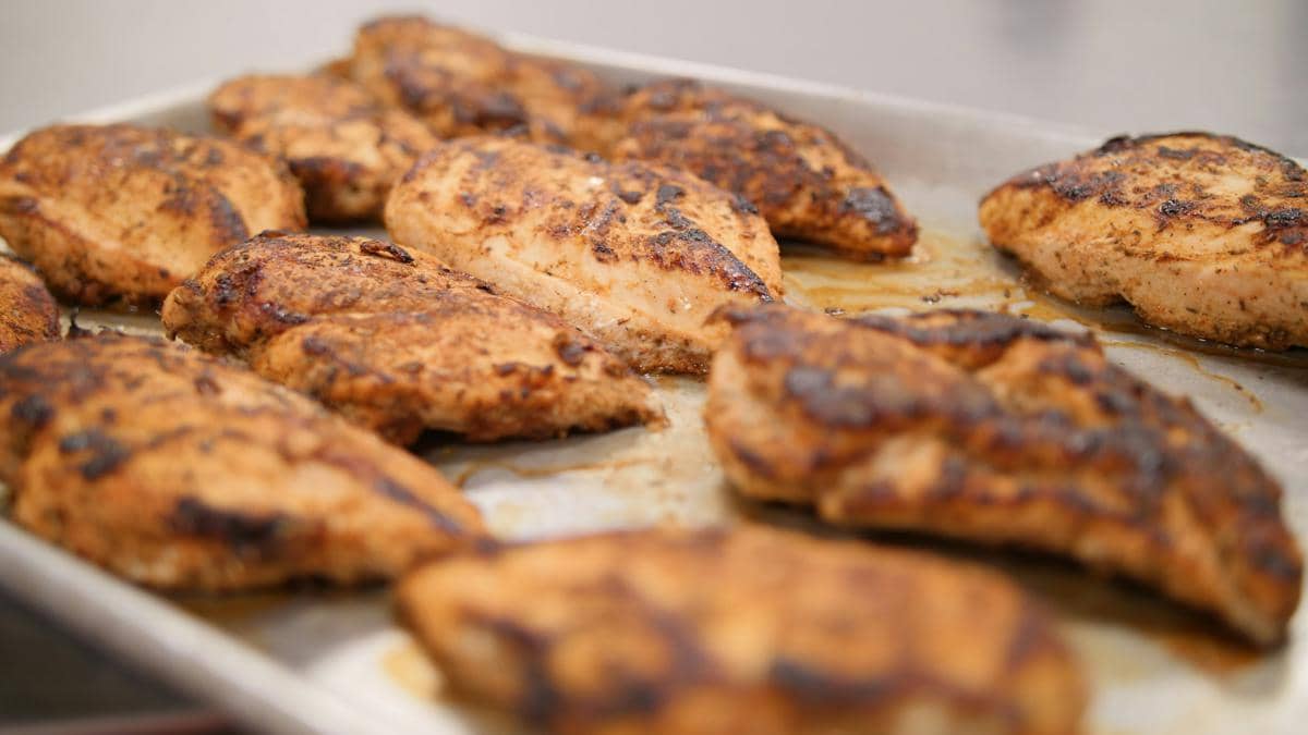 Beberapa potong dada ayam panggang berwarna kecokelatan di atas loyang logam dengan bumbu yang meresap sempurna.
