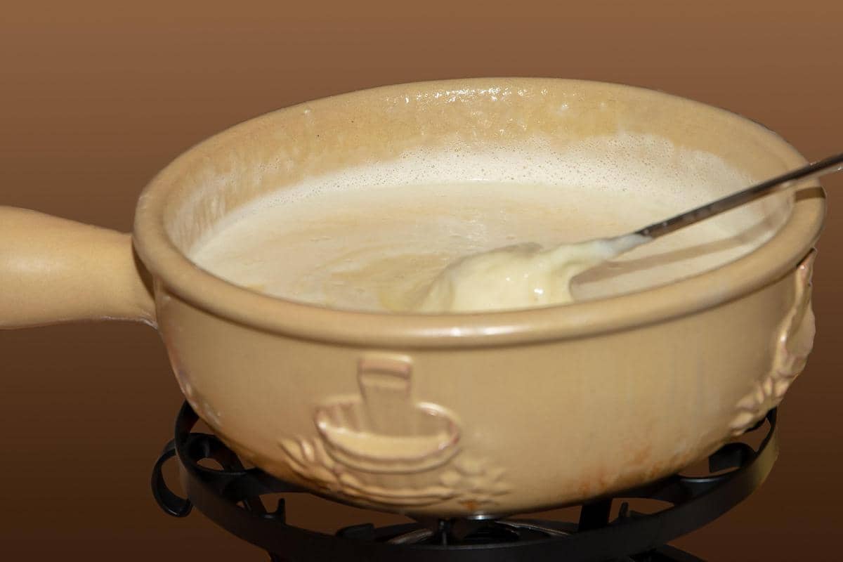 Panci keramik berisi lelehan saus keju hangat dengan sendok logam, digunakan sebagai saus untuk nachos keju.