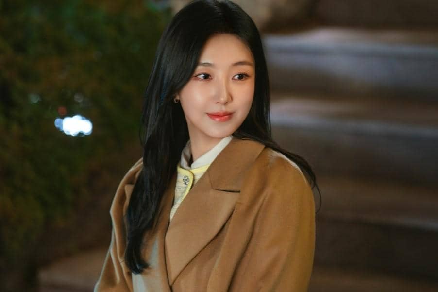 Seorang wanita berambut panjang mengenakan mantel cokelat tersenyum lembut di malam hari dalam cuplikan drama Reborn Rookie.