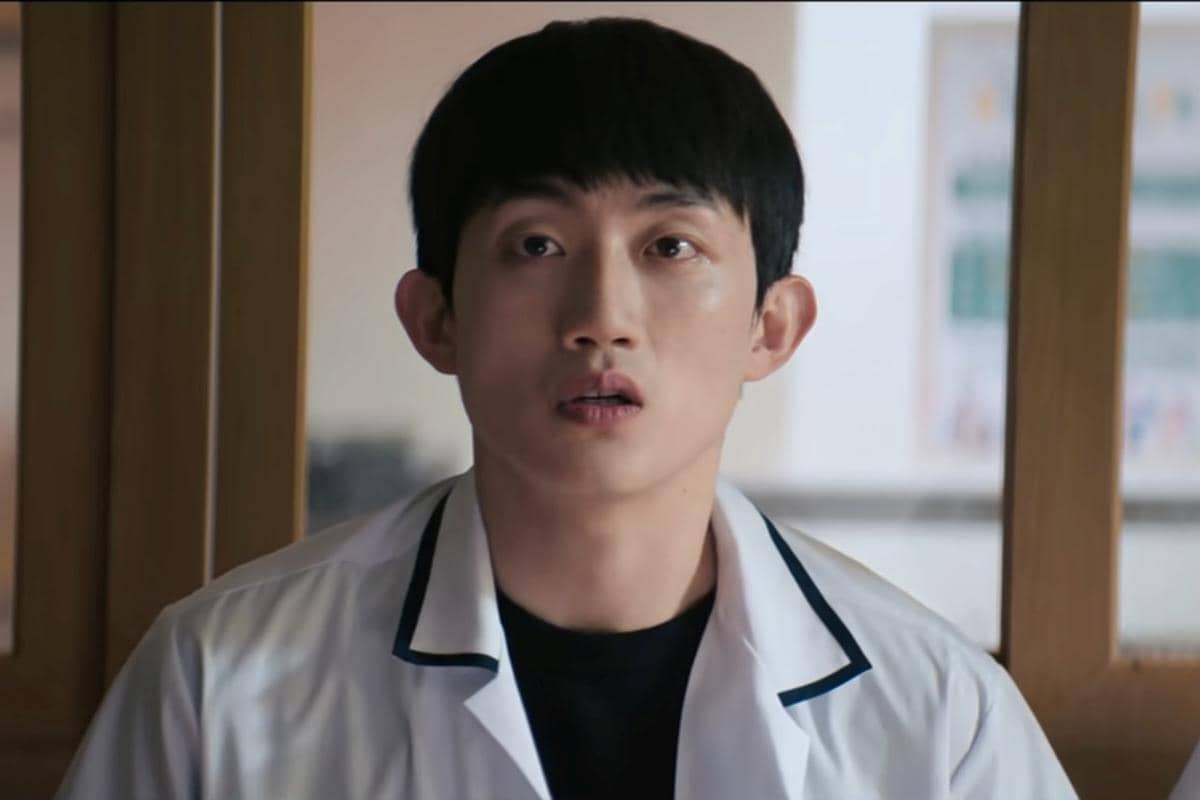 Seorang pria mengenakan seragam sekolah putih dengan kerah hitam tampak menatap ke depan di adegan drama Korea Teach You a Lesson.