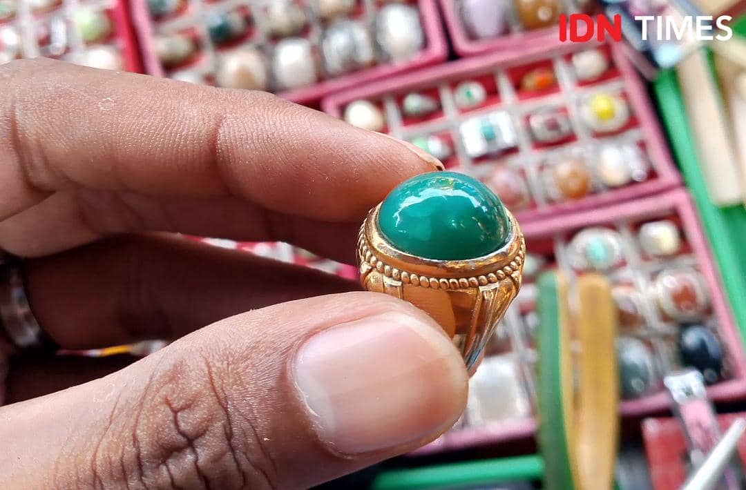 Cincin batu bacan majiko berwarna hijau kebiruan dengan bingkai logam emas dipegang oleh tangan di pasar perhiasan Purwokerto.