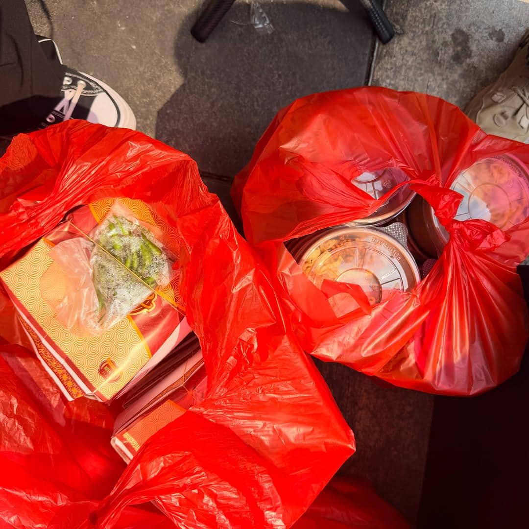 Dua kantong plastik merah berisi kotak makanan dan minuman siap saji diletakkan di atas permukaan jalan beraspal.