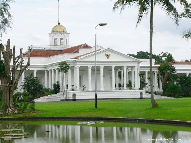 Bangunan bergaya kolonial berwarna putih dengan pilar tinggi dan kubah emas di atapnya, dikelilingi taman hijau dan kolam air di Bogor.