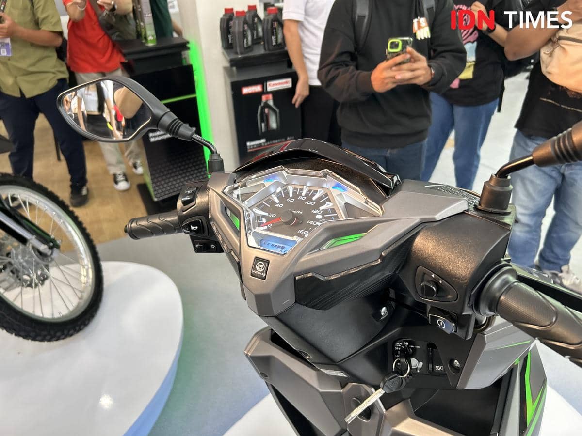 Panel speedometer Kawasaki Brusky 125 dengan desain modern berwarna hitam dan hijau, terlihat di area pameran motor dengan beberapa pengunjung di sekitarnya.