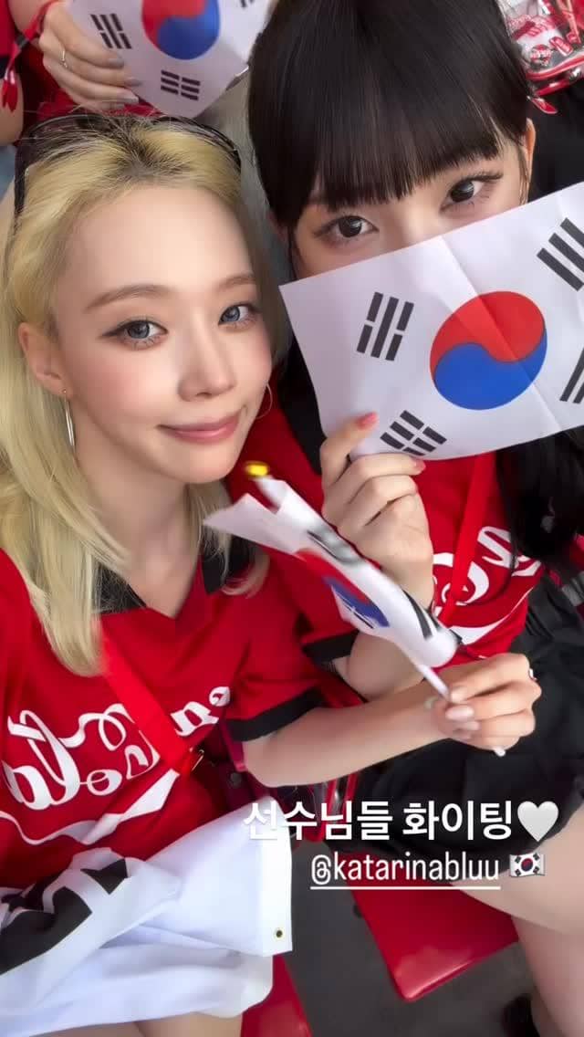 Dua perempuan mengenakan jersey merah Korea Selatan sambil memegang bendera nasional di tribun penonton Piala Dunia 2026 di Meksiko.
