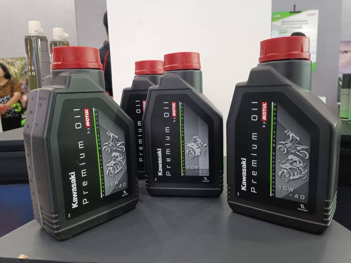 Beberapa botol oli Kawasaki Premium Oil hasil kolaborasi dengan Motul dipajang di atas meja dengan latar suasana pameran.