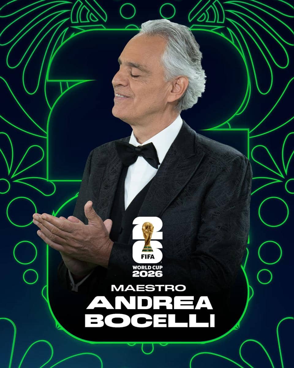 Seorang pria berjas hitam dengan dasi kupu-kupu berpose sambil tersenyum di depan latar bertema Piala Dunia FIFA 2026.