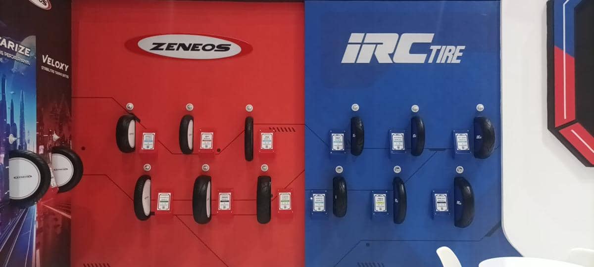 Deretan ban motor merek Zeneos dan IRC Tire dipajang di dinding berwarna merah dan biru dengan label ukuran dan spesifikasi produk.