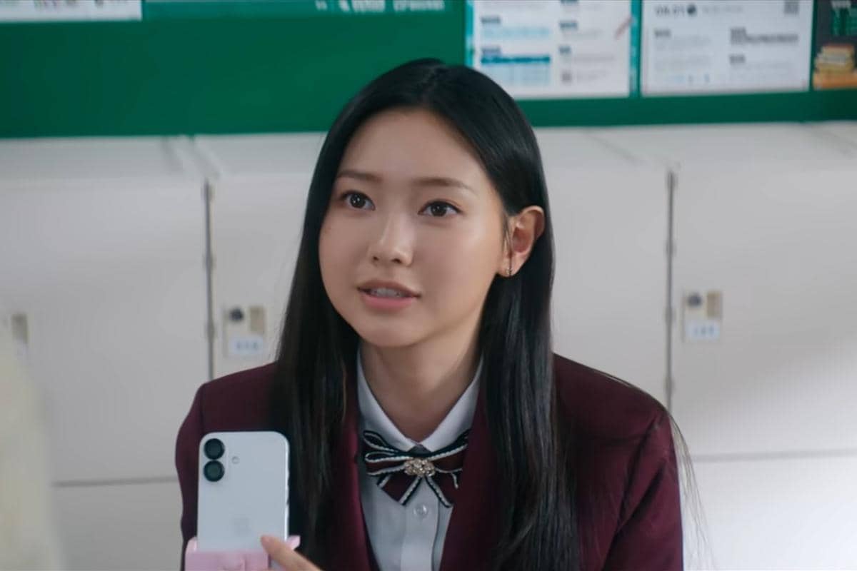Seorang siswi berseragam sekolah marun memegang ponsel di ruang kelas dalam adegan drama Korea Teach You a Lesson.