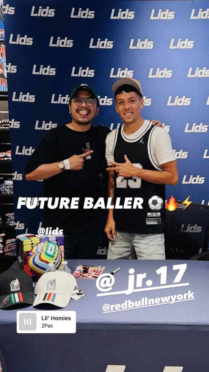 Dua pria berpose bersama di depan latar bertuliskan Lids, salah satunya mengenakan topi dan jersey hitam dengan angka 23.