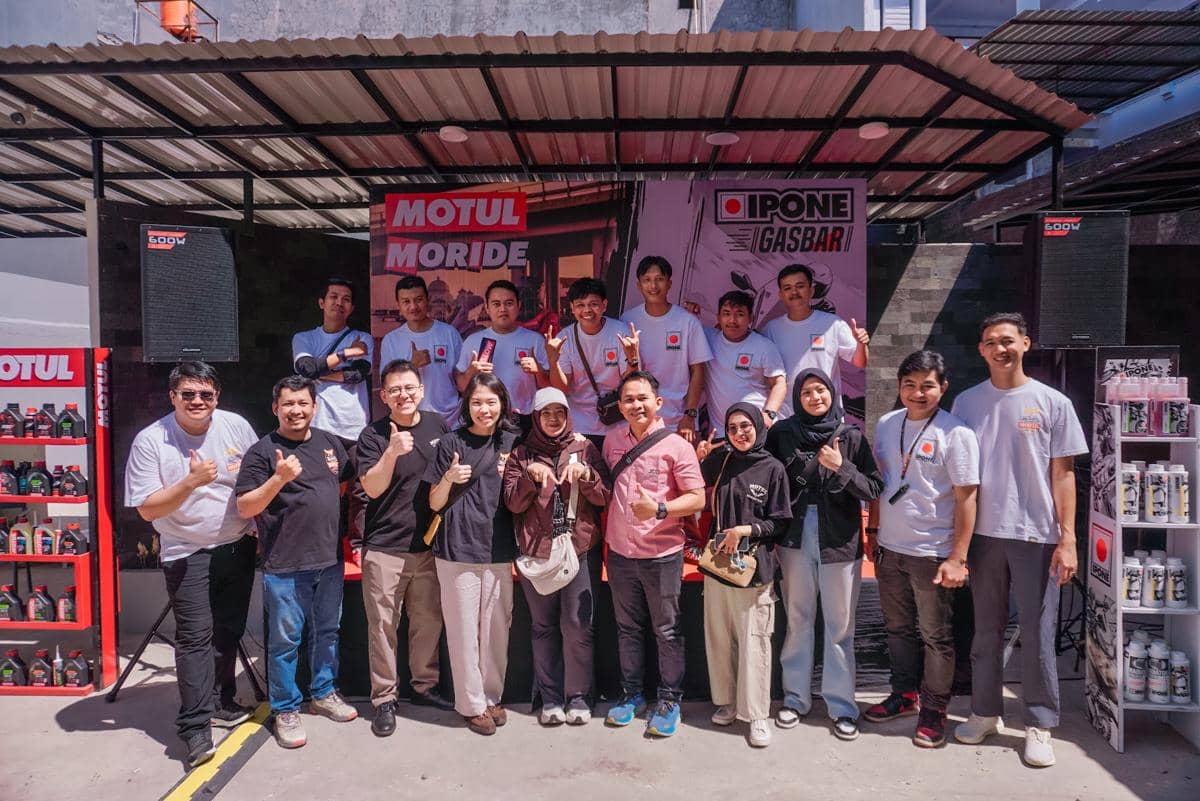 Sekelompok peserta berfoto bersama di acara penggantian oli yang disponsori oleh Motul dan IPONE di area luar ruangan.