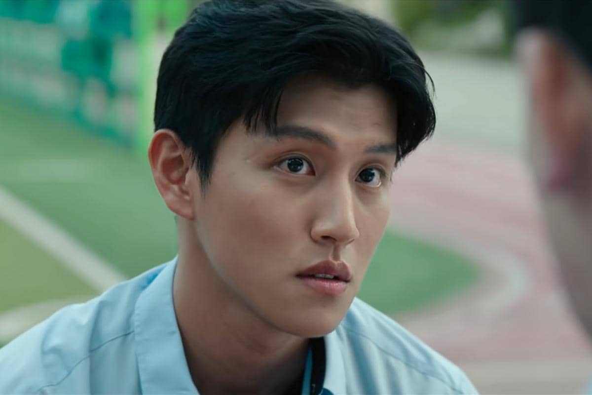 Seorang pria muda mengenakan seragam biru muda menatap serius ke arah seseorang di depannya dalam adegan drama Korea Teach You a Lesson.