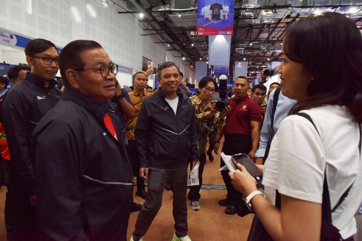 Seorang pejabat pemerintah berbicara dengan peserta acara di dalam ruangan pameran yang ramai dengan sejumlah orang dan media.