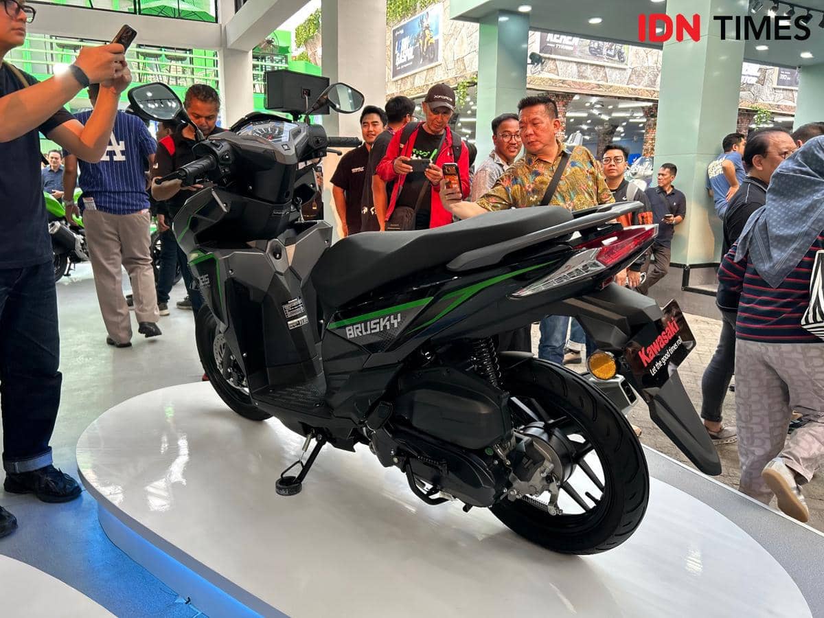 Motor matik Kawasaki Brusky 125 berwarna hitam dan hijau dipamerkan di atas panggung dengan banyak pengunjung yang melihat dan memotret.
