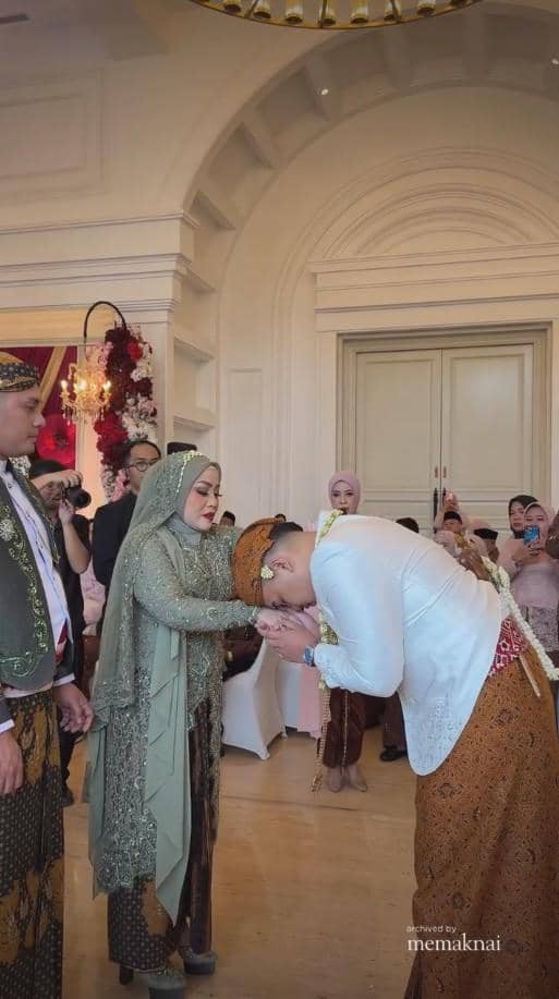 Mempelai pria bersujud sungkem kepada orang tua dalam upacara pernikahan adat Jawa di dalam ruangan elegan dengan tamu yang menyaksikan.