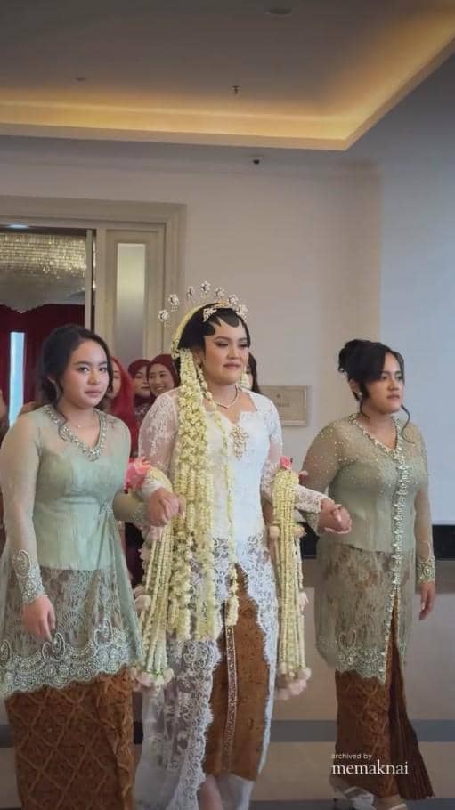 Pengantin wanita mengenakan kebaya putih dan siger Sunda berjalan diapit dua pendamping berkebaya hijau dalam prosesi pernikahan.