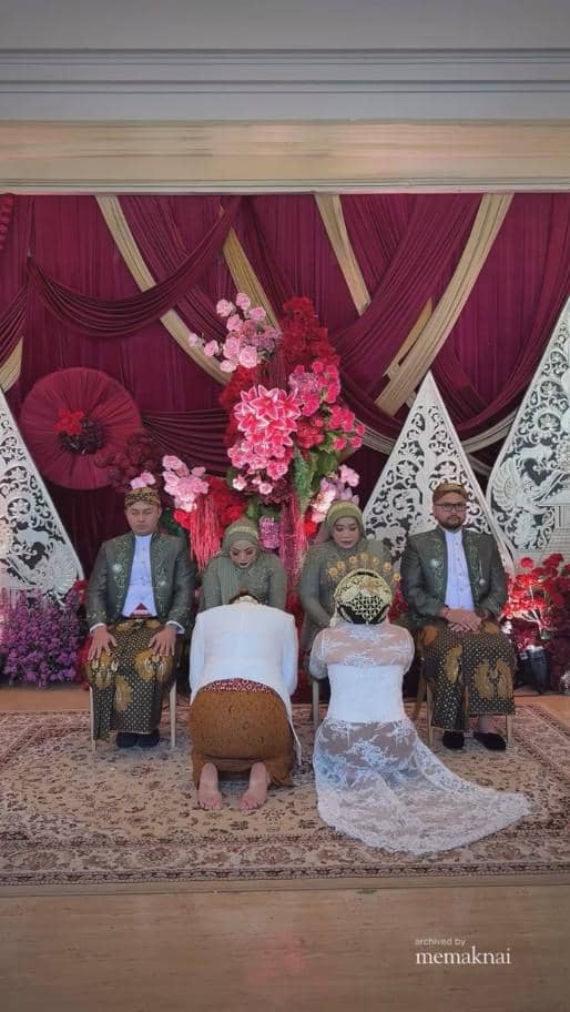Prosesi pernikahan adat Jawa dengan pengantin wanita bersujud di hadapan orang tua di pelaminan berhias bunga merah dan ungu.